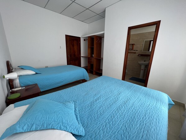 A room with two beds, a wooden wardrobe, and a bathroom visible through a doorway.