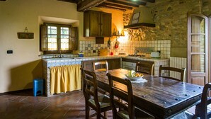 A rustic kitchen with a wooden table, chairs, and a stone wall. - Apartment/ flat - Chianni (Chianni)