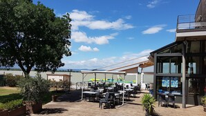 Un patio al aire libre con mesas y sillas, un área de estar cubierta y vista al agua.