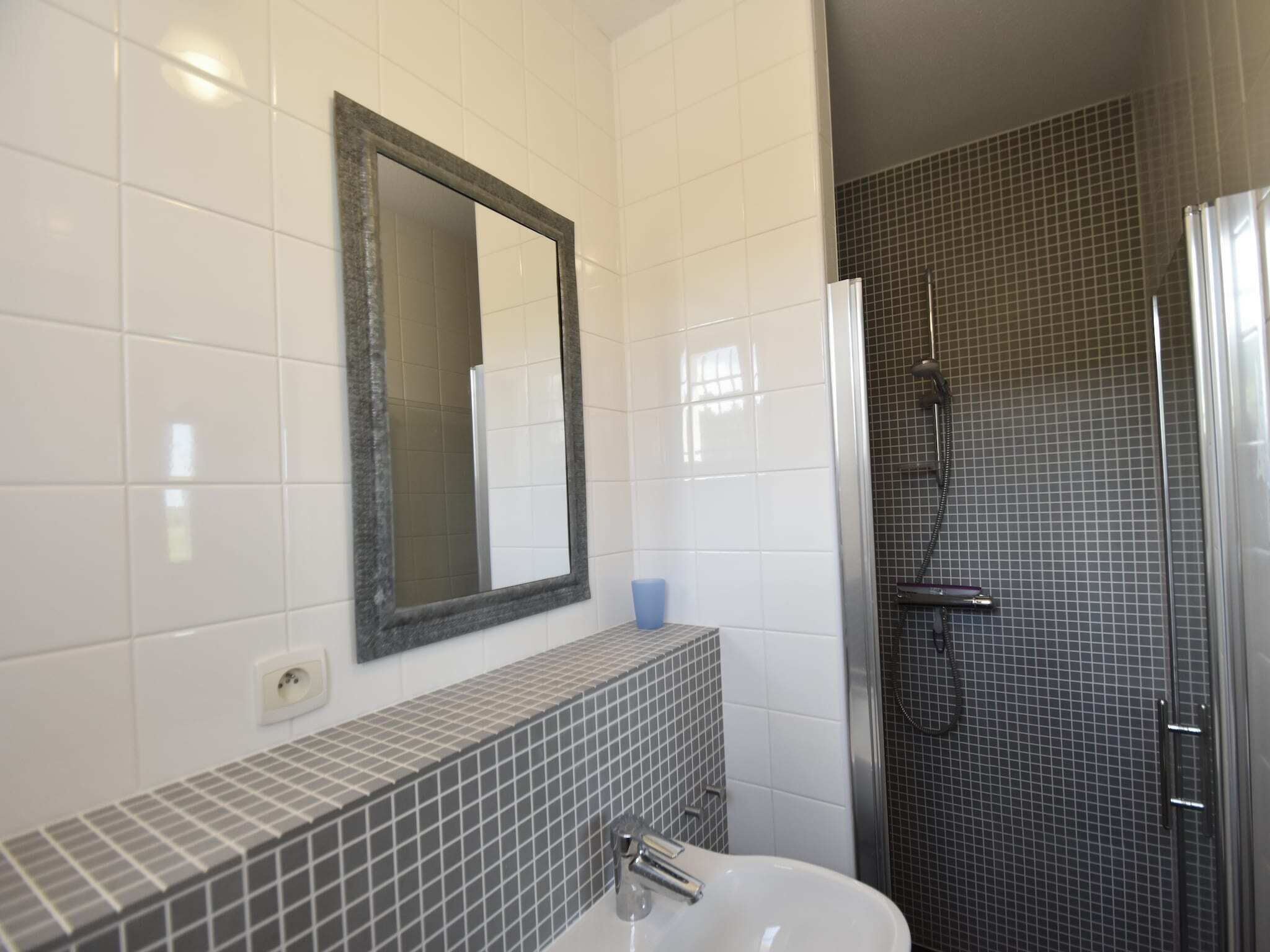 Une salle de bain avec un mur carrelé, un lavabo, un miroir et un espace douche.