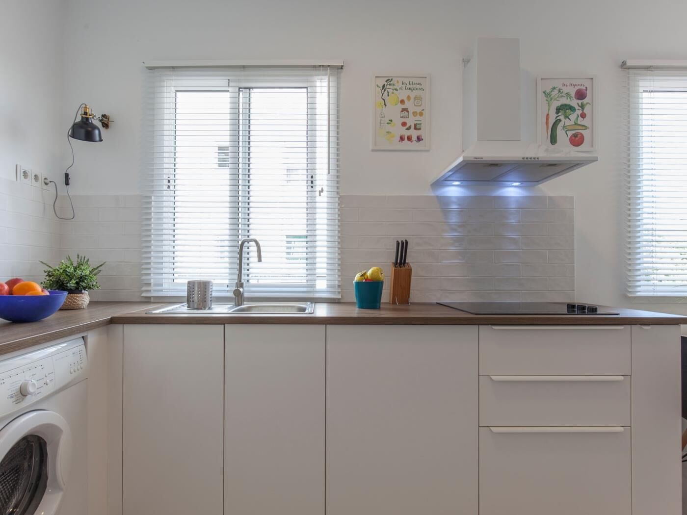 A modern kitchen with white cabinets, a built-in washing machine, a sink, and a window with blinds.
