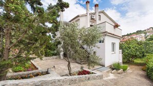 Edifici blanc amb teulada inclinada, envoltat de vegetació i un camí de pedra.