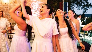 Un groupe de personnes vêtues de robes blanches lors d’un événement en plein air, avec des murs en pierre et des guirlandes lumineuses.