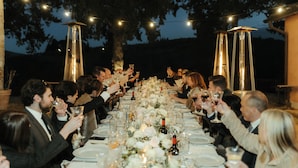 A long dining table with guests seated, surrounded by string lights and tall, narrow light fixtures. - Exclusive Estate | Personal Concierge & Heated Pool (impruneta)