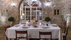 A dining table set for a meal in a stone-walled room with a large arched window. - Exclusive Estate | Personal Concierge & Heated Pool (impruneta)