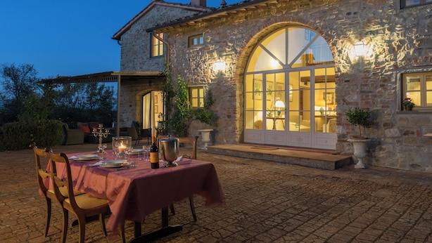 A stone building with a dining area set up outside, featuring a table with a tablecloth, chairs, and a candle. - Exclusive Estate | Personal Concierge & Heated Pool (impruneta)