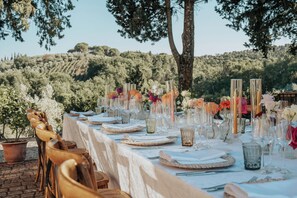 Un espace de restauration en plein air avec une longue table dressée pour un repas, entouré d’arbres et de collines.