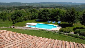 Una piscina con sillas azules, rodeada de exuberante vegetación y colinas al fondo.