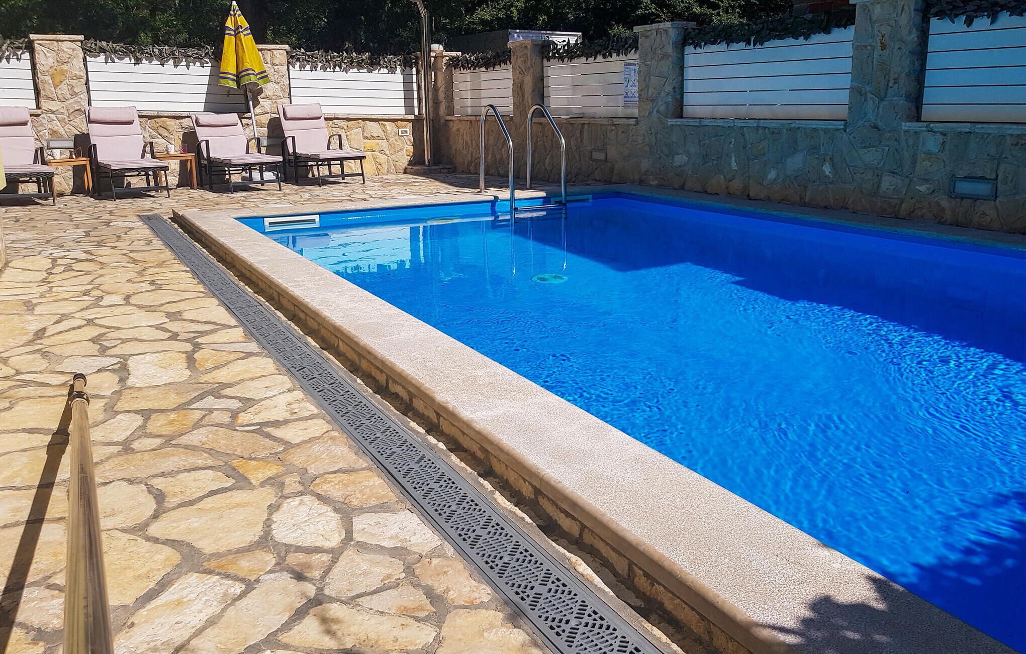 A swimming pool with a stone deck, lounge chairs, and a yellow umbrella.