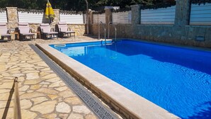 A swimming pool with a stone deck, lounge chairs, and a yellow umbrella. - Luxurious home in Bribir (Bribir)