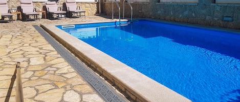 A swimming pool with a stone deck, lounge chairs, and a yellow umbrella.