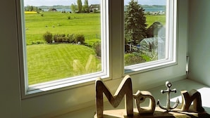 Una ventana con vista a un paisaje verde, un adorno de ancla de madera y un cielo despejado.