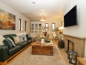 A living room with a leather sofa, a wooden coffee table, a fireplace, and a flat-screen TV mounted on the wall.