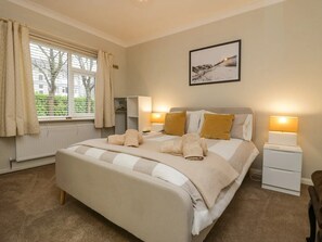 A neatly arranged bedroom with a bed, bedside lamps, a radiator, and a window with curtains.