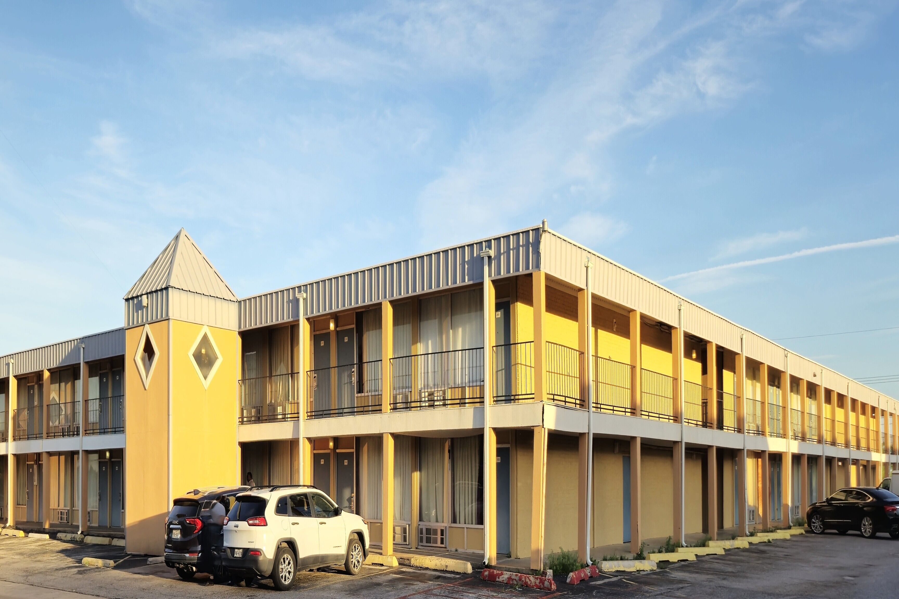 A multi-story motel with a central courtyard, featuring a flat roof and a triangular tower.