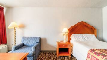 A hotel room with a bed, a chair, a nightstand with a lamp, and a patterned carpet.