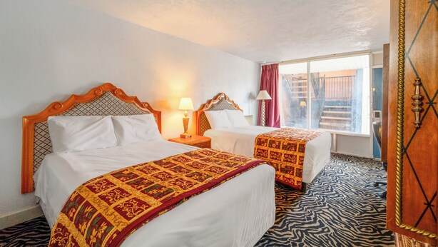 A hotel room with two beds, each with a patterned bedspread, a wooden headboard, and bedside lamps. - Castle Inn & Suites by OYO Lawton (Lawton)