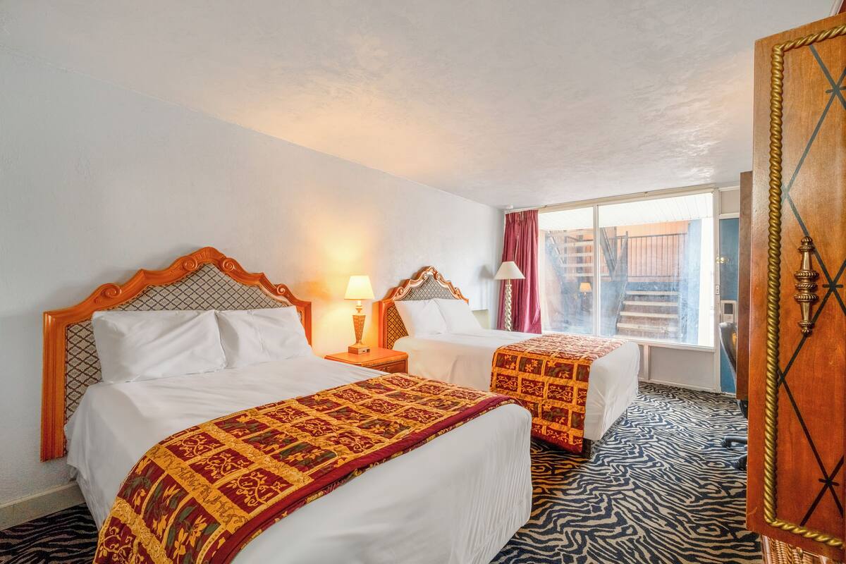 Habitación de hotel con dos camas, cada una con una colcha estampada, cabecero de madera y lámparas de noche.