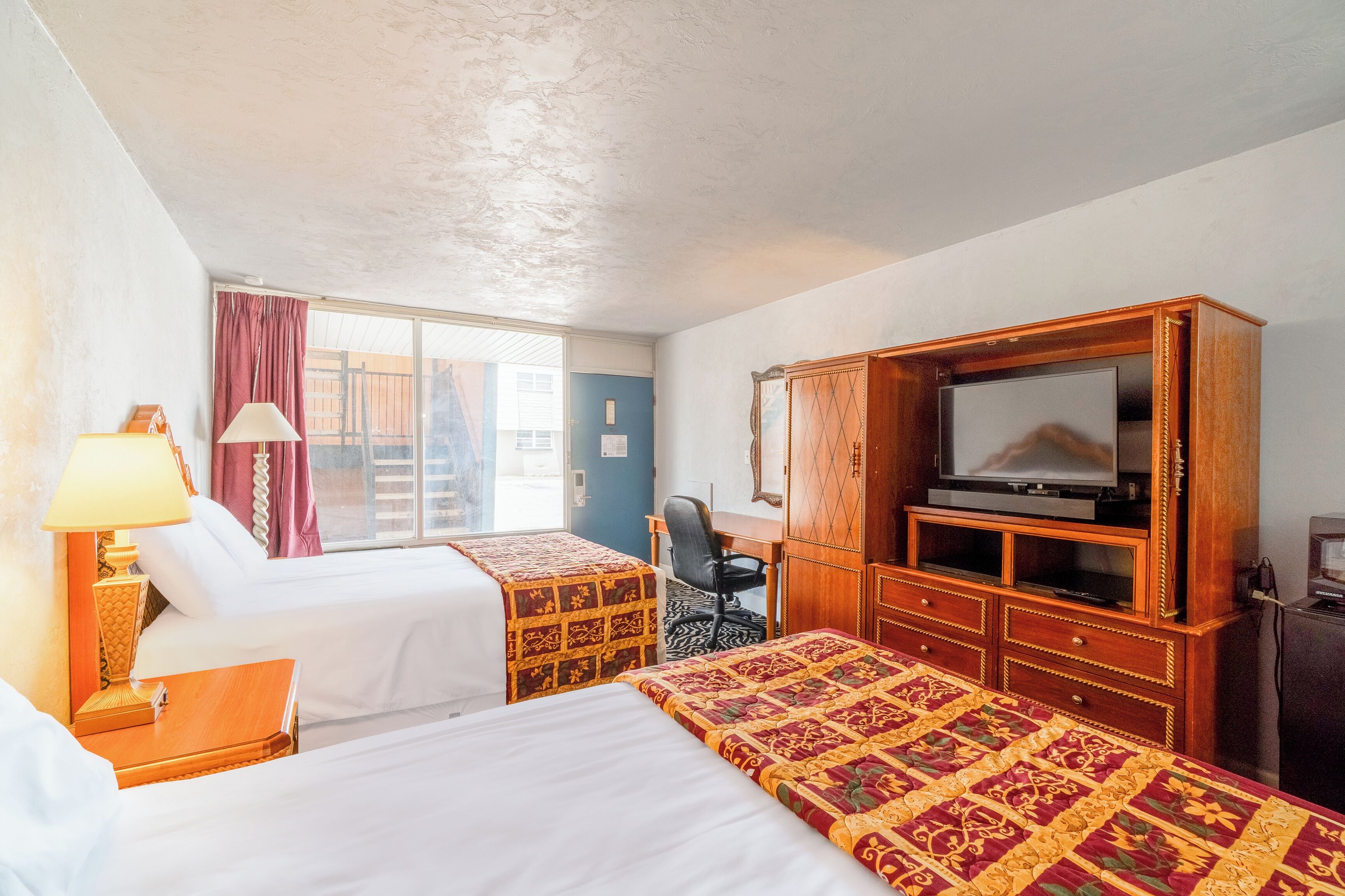 A hotel room with two beds, a TV, a desk, and a chair.