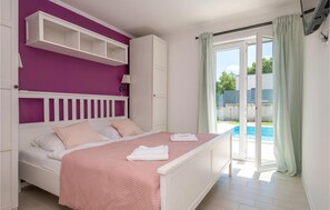 A bedroom with a bed, a white wardrobe, a purple wall, a window with curtains, and a view of a swimming pool. - Luxurious home in Marici with sauna (Marici)
