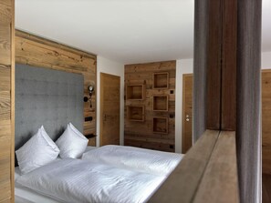 A bedroom with a bed, a grey headboard, wooden walls, and a door with square cutouts. - 2 room apartment no. 2 - Alt Filzmoos, Das Anja (Filzmoos)