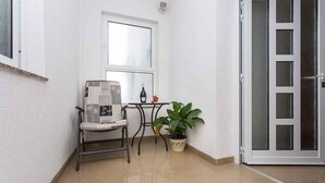 Ein kleiner Balkon mit einem Stuhl, einem Tisch, einem Blumentopf und einer Schiebeglastür.
