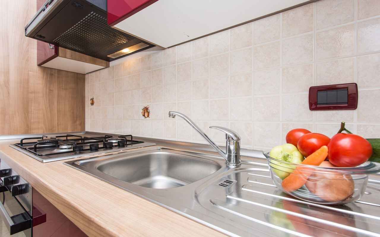 A modern kitchen with a gas stove, stainless steel sink, and a bowl of fresh vegetables.