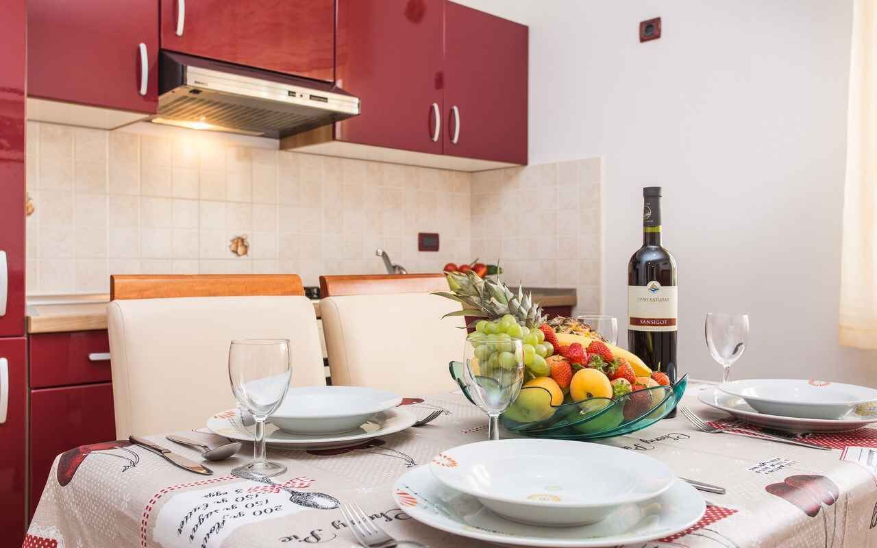 Een eettafel gedekt met borden, bestek en een schaal met fruit. Er staat ook een fles wijn en een glas op tafel.