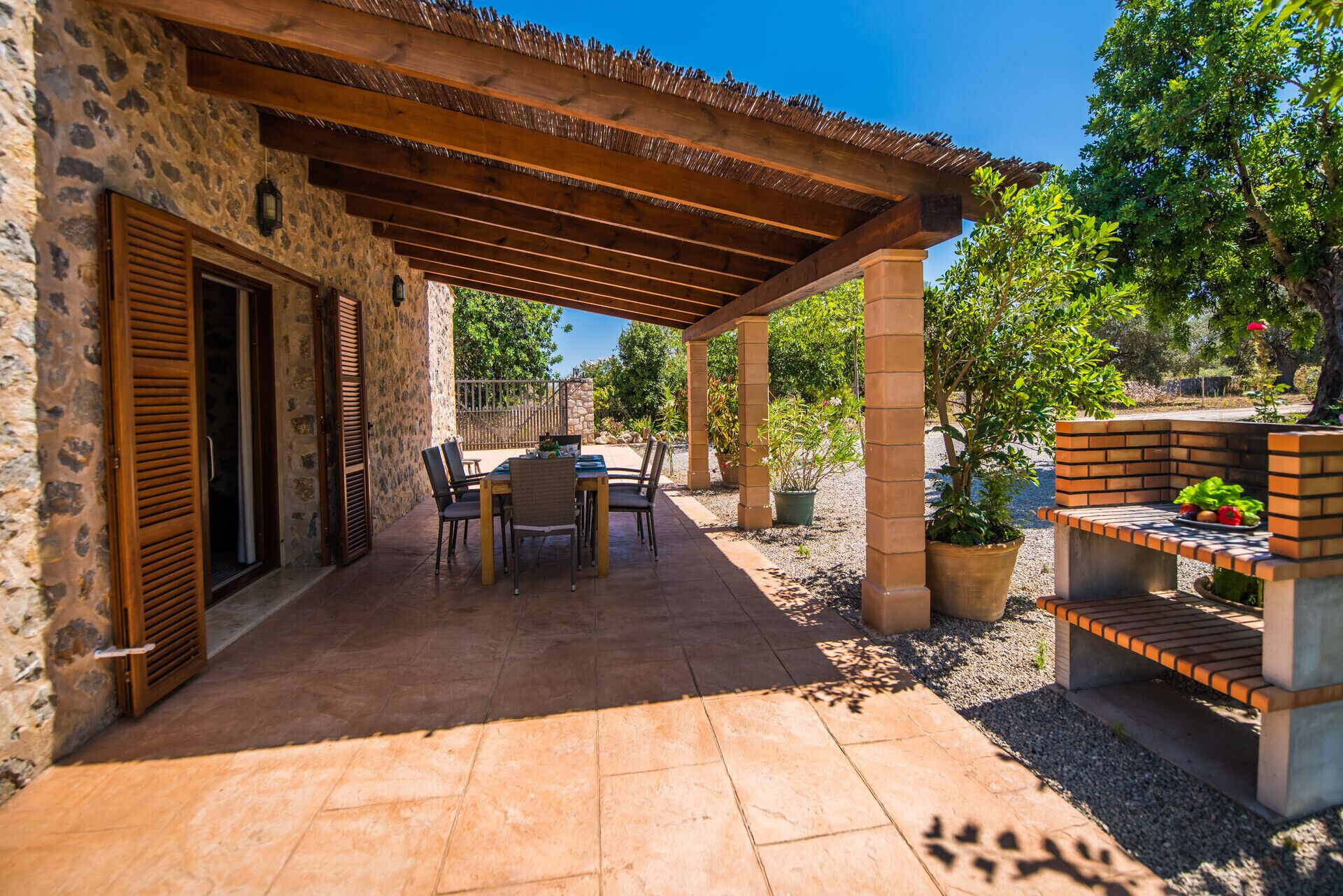 A covered patio with stone walls, a table with chairs, and a brick barbecue area.
