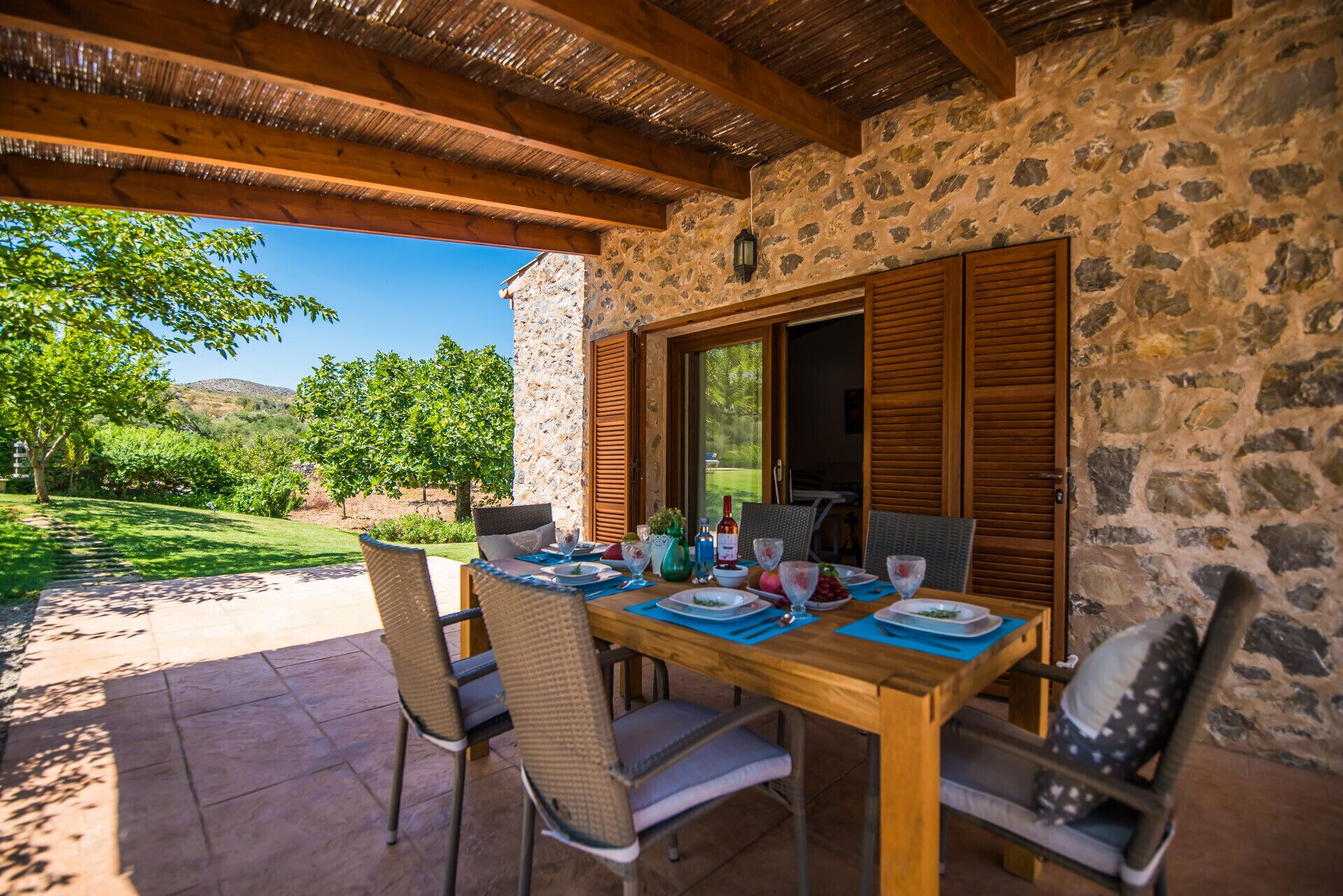 Un espace de restauration extérieur, délimité par des murs de pierre, avec une table en bois dressée pour quatre personnes, entourée de chaises en osier.