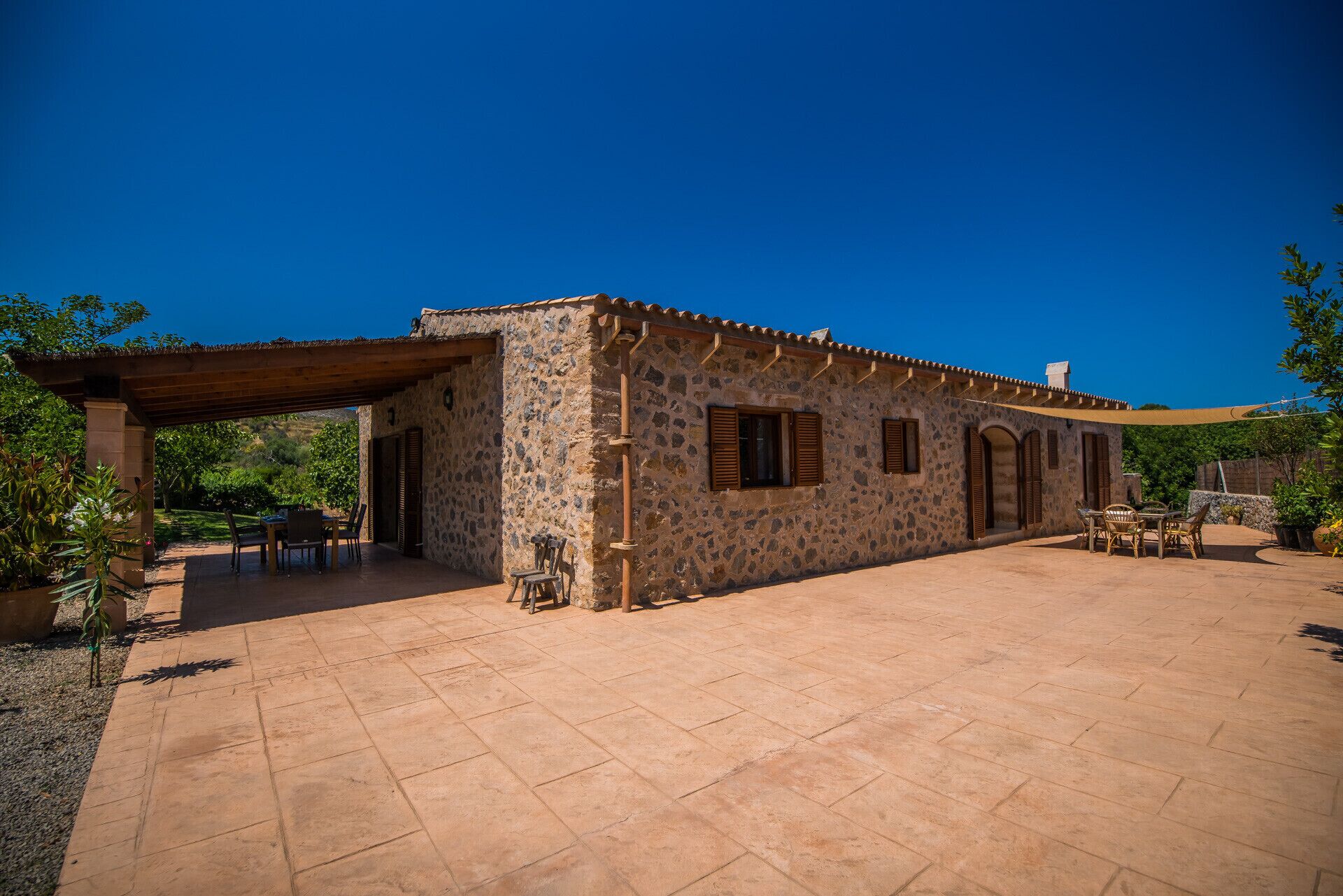 A stone building with a tiled patio, outdoor furniture, and a clear blue sky.