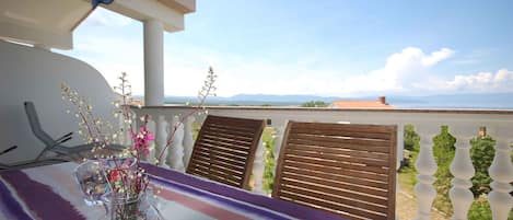 Un balcón con vistas a montañas distantes, un florero con flores y sillas de madera.