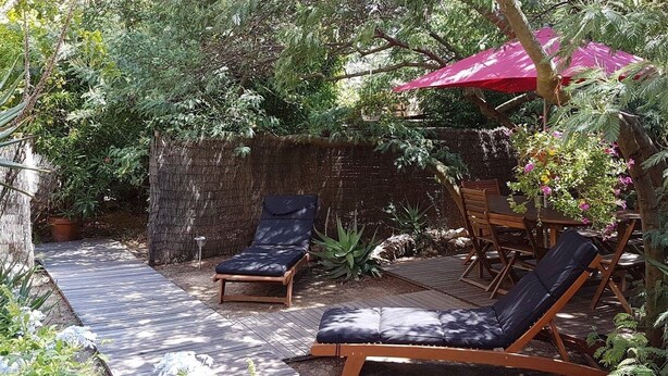 An outdoor seating area with two lounge chairs and a red umbrella, surrounded by dense foliage and a wooden deck. - Studio Orsoni - See View (Calvi)