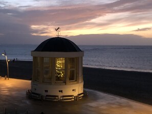 Un phare surmonté d’un dôme et d’une girouette, situé sur une plage avec l’océan en arrière-plan.