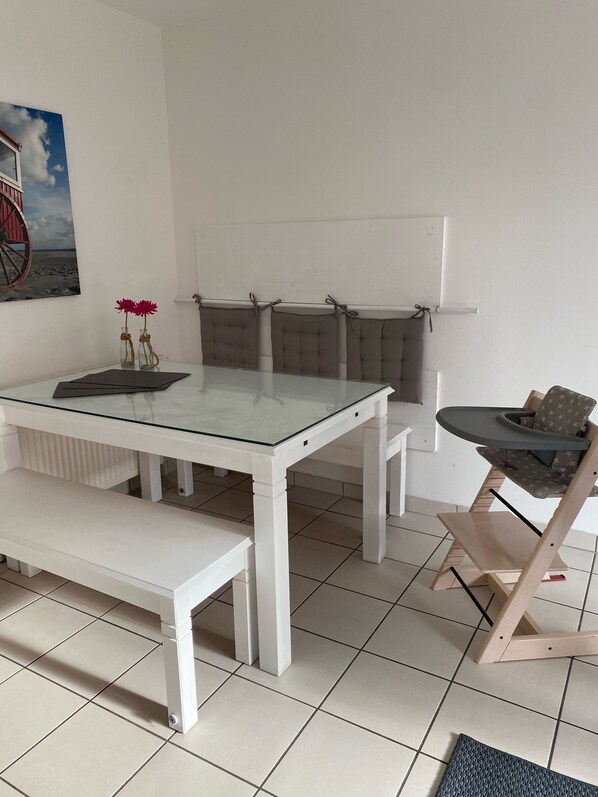 A white dining table with a glass top, a bench, and a high chair with a patterned seat.
