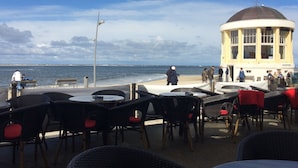 An outdoor seating area with tables and chairs, a view of the sea, and a building with a dome.