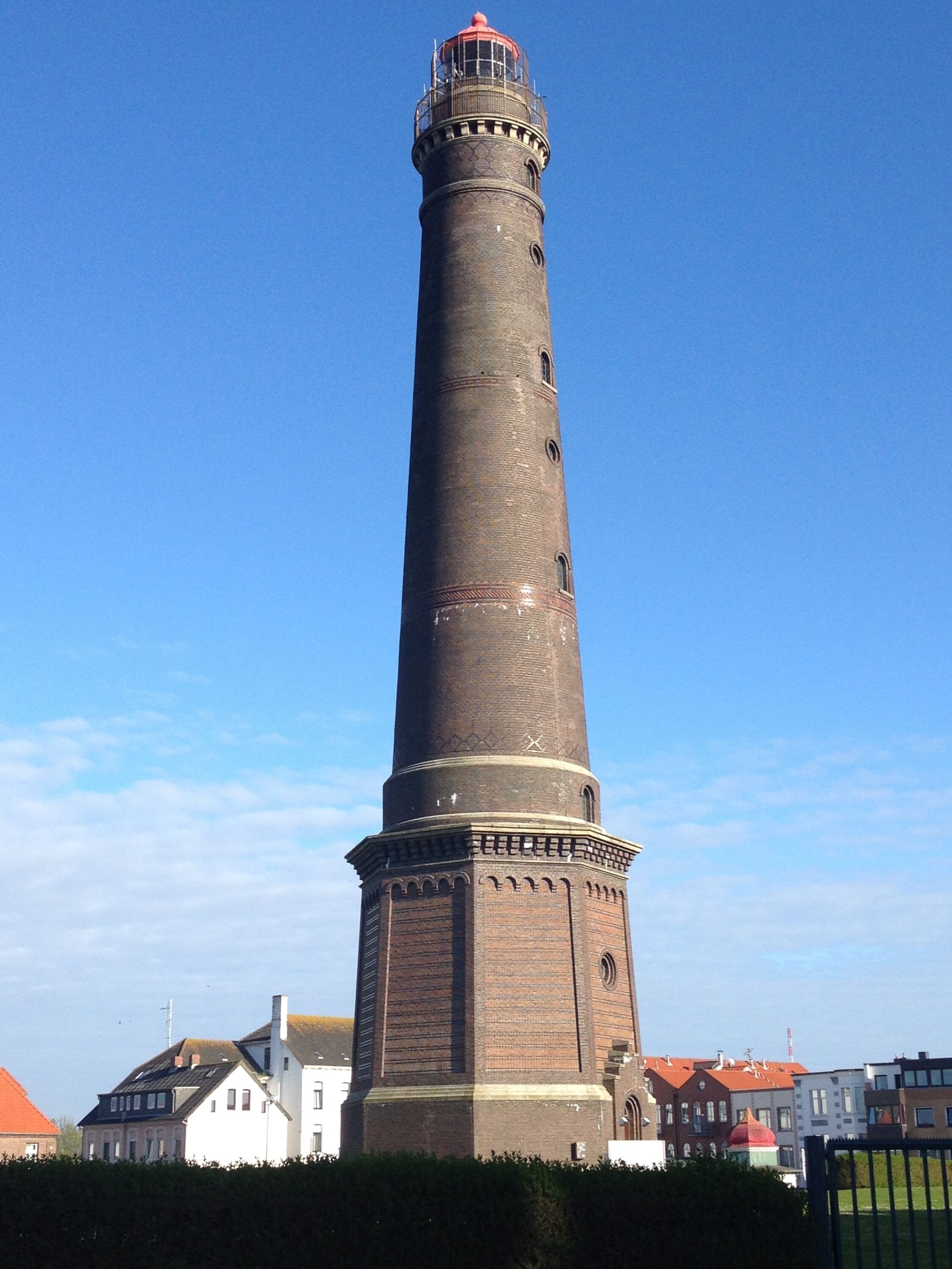 Une haute tour en briques surmontée d’un toit rouge, et un bâtiment plus petit aux murs blancs et au toit rouge, situé au premier plan.