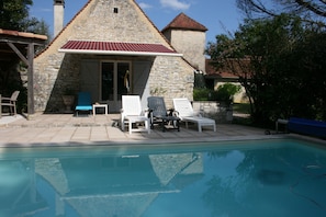 Un bâtiment en pierre avec un toit rouge, une piscine et plusieurs chaises longues.