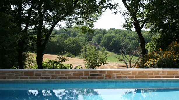 A swimming pool with a stone wall and trees in the background. - Former sheepfold renovated, quiet, with heated pool. (Montgesty)