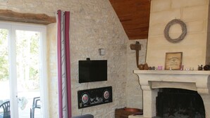 A living room with a stone wall, a fireplace, a sofa, and a television. - Former sheepfold renovated, quiet, with heated pool. (Montgesty)