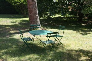 Une table et des chaises en métal de couleur verte sont disposées à l’extérieur, près d’un arbre.