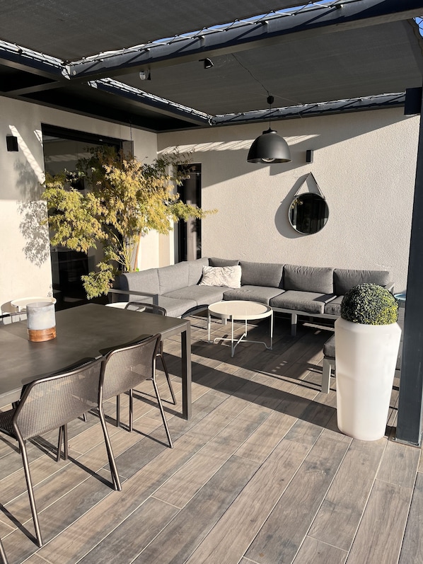 Um pátio externo com mesa de jantar, cadeiras, um sofá e uma mesa redonda.