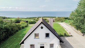 Una casa blanca con un techo pronunciado, una chimenea y vista al mar.