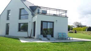 A modern two-story house with a balcony, large windows, and a grassy lawn with outdoor seating. - House exceptional sea view on the Pink Granite Coast (Penvénan)