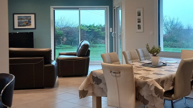 A modern dining area with a table set for four, surrounded by chairs. There is a television on the left and a large window providing a view of the outdoors. - House exceptional sea view on the Pink Granite Coast (Penvénan)