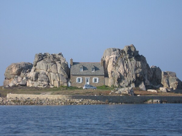 A stone house with a sloped roof, situated on a rocky outcrop by the sea.