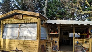 Een rustieke houten chalet met een bord waarop 'La Cabane A Loulou' staat, met een groot raam, een houten bankje met dennenappels en een kleine tafel.