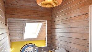 En stuga med träpanel, ett sluttande tak, en säng med kuddar, en väggklocka och ett fönster med utsikt.