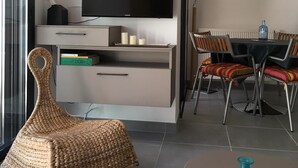 A modern living room with a flat-screen TV, a dining area with a table and chairs, and a large window.