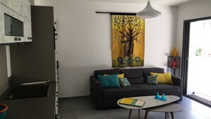 A modern living room with a dark sofa, colorful cushions, a small table with a tray, and a large wall painting of a tree and birds.